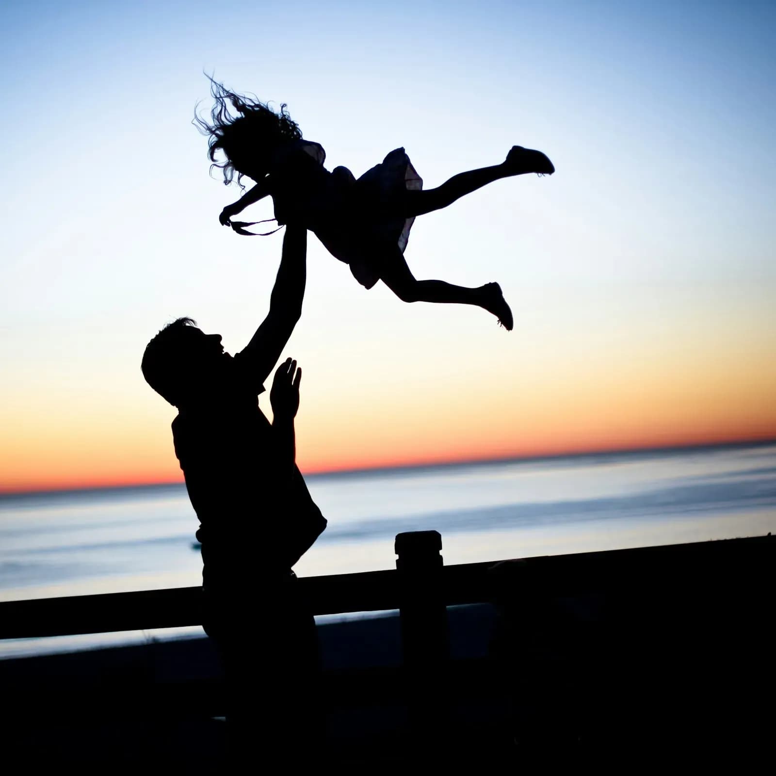 A parent lifting a child into the air at sunset