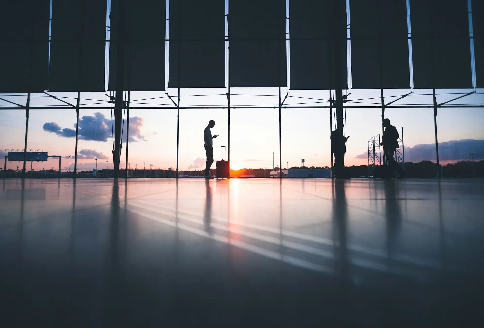 Travellers silhouetted against an airport window at sunset